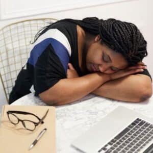 Woman resting her head on a table next to a laptop, appearing fatigued